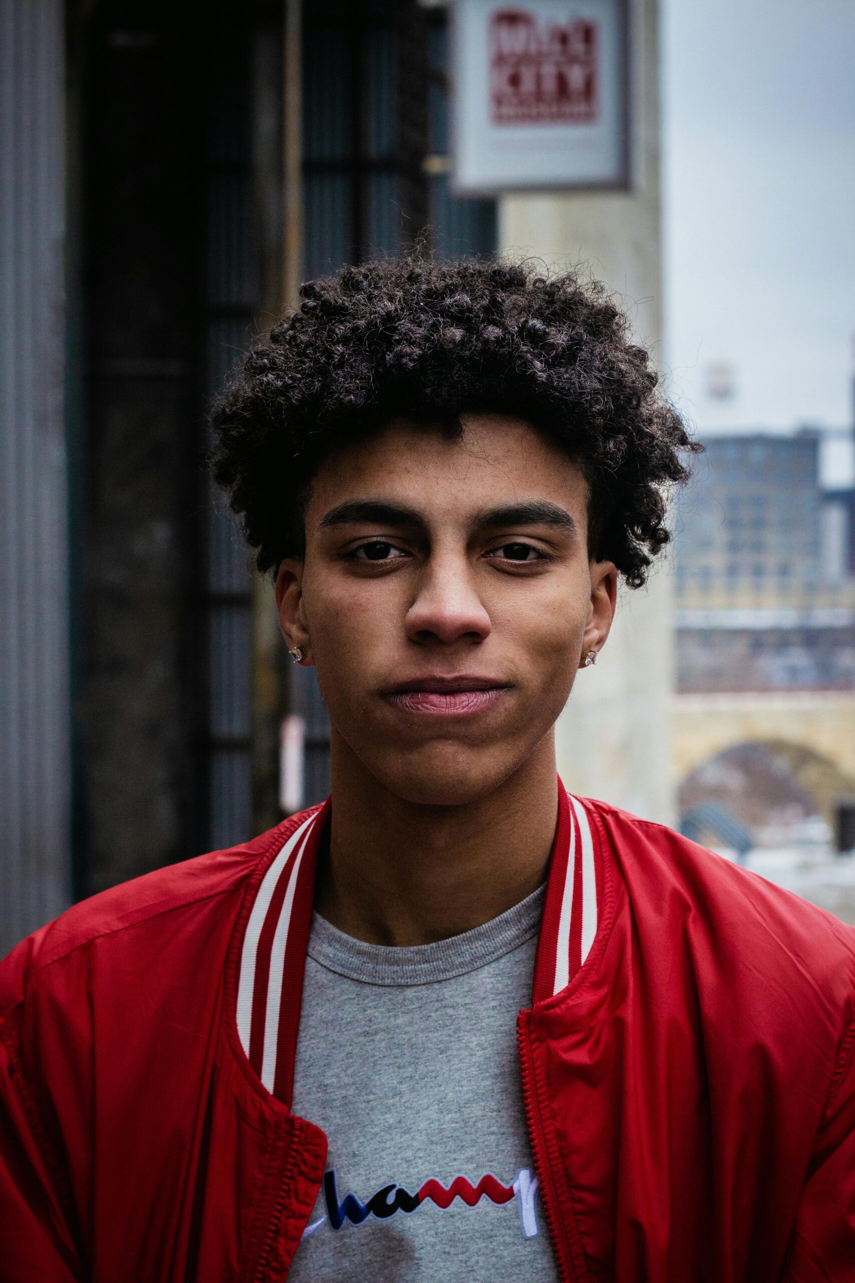 Portrait of a young man in a red jacket, captured in an urban setting with a solemn expression.